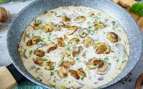 Cremige Rahmsauce mit frischen Champignons, verfeinert mit Petersilie, in einer Pfanne.