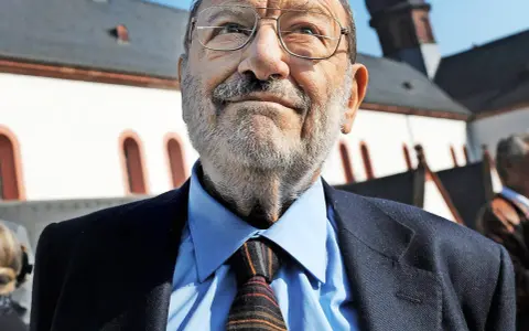 Porträt eines älteren Mannes mit Brille, Schnurrbart und Bart, der einen Anzug und eine Krawatte trägt.