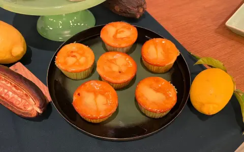 Sechs Zitronenmuffins mit glänzender Glasur auf einem Teller, daneben frische Zitronen und eine Kakaofrucht. Ein leckeres zitronenmuffins rezept!