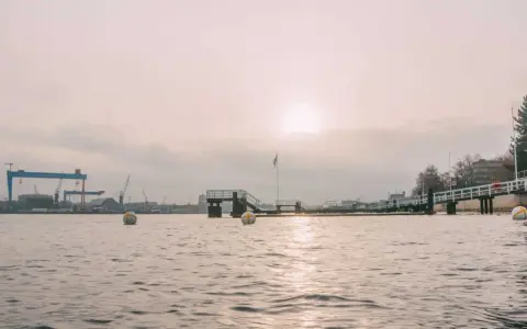 Kiel im Winter: Hafenkräne und eine Mole im nebligen Licht. Bojen treiben auf dem ruhigen Wasser.