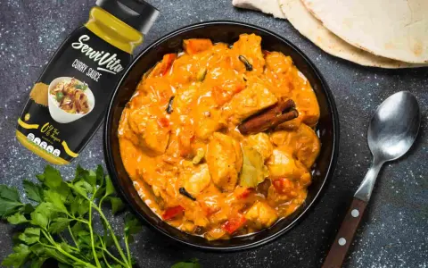 Bol de pollo al curry cremoso con especias, salsa y pan naan al lado.