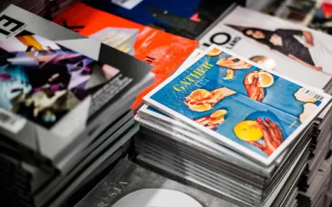 Stosy magazynów, jeden z nich z okładką "GATHER" i pomarańczami, gdzie każdy detal, od tekstury owoców po odbicia światła, podkreśla piękno koloru spotowego.