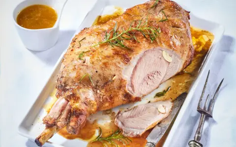 Un gigot d'agneau rôti, doré et juteux, garni de romarin et d'ail, servi avec sa sauce. Un délice à partager.