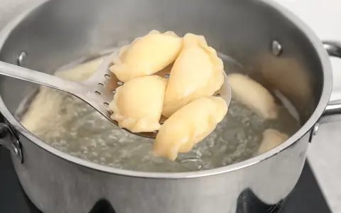 Pierogi gotujące się w garnku, wyjmowane łyżką cedzakową.