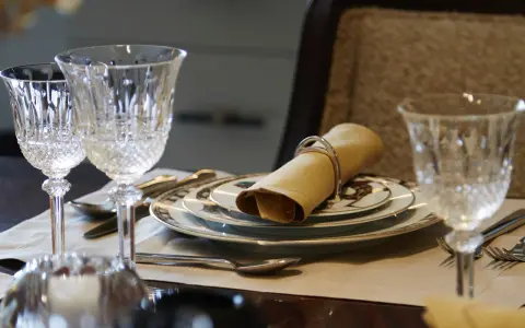 Verre à pied taillé, assiettes décorées, serviette en tissu joliment pliée : une table dressée pour le service à la française.