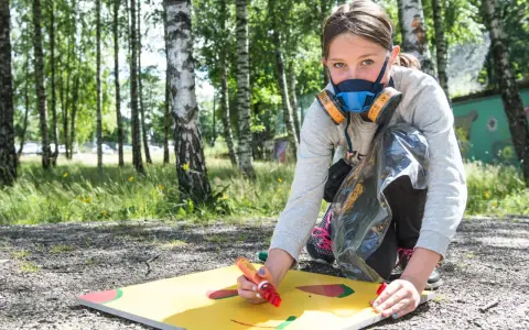 Ung flicka med munskydd skapar graffiti på papper utomhus.
