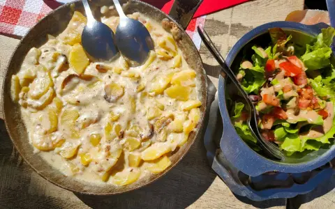 Plat de pommes de terre crémeuses, une spécialité auvergnate, servi dans une poêle avec une salade fraîche.
