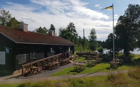 Mysigt tiveden boende med uteservering vid vattnet. En svensk flagga vajar i vinden.