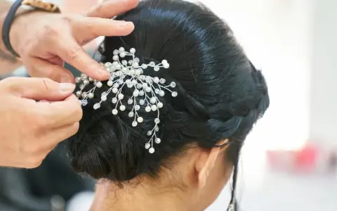 Manos expertas ajustan un tocado de perlas y cristales a un juvenil recogido de boda, creando un look elegante y romántico.