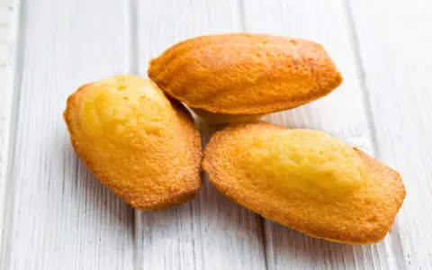 Trois délicieuses pâtés à madeleine dorées sur une planche en bois blanc.