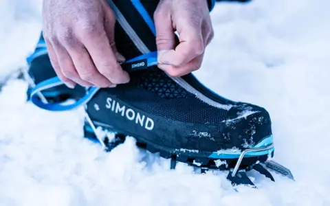Dłonie zapinają raki do butów w śniegu, przygotowując się do wspinaczki w góry.