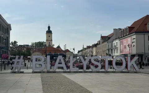 #Białystok na Rynku Kościuszki. Wielkie litery tworzą napis, w tle kamienice i wieża ratuszowa.