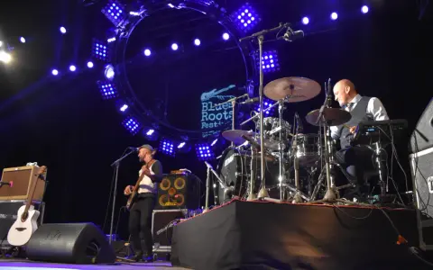 Un groupe joue du blues musique sous un grand cercle lumineux. Un bassiste à gauche, un batteur à droite.