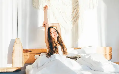 Eine Frau streckt sich im Bett aus, umgeben von weißer Bettwäsche. Sie genießt den Morgen, bereit, zusammen einzuschlafen und den Tag zu beginnen.