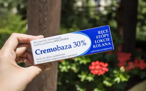 Dłoń trzyma opakowanie kremu Cremobaza 30%, przeznaczonego do pielęgnacji suchej, zrogowaciałej skóry dłoni, stóp, łokci i kolan.