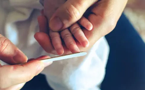 Mani adulte limano delicatamente le unghie di un neonato, un momento di cura che mostra quando si possono tagliare le unghie ai neonati.