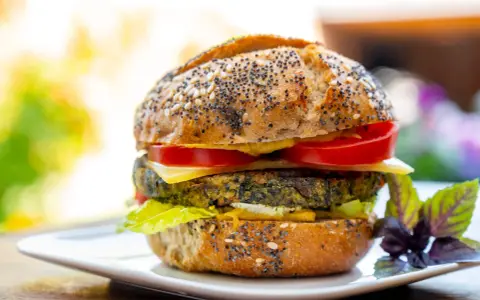 Deliciosa hamburguesa de espinacas con pan de semillas, queso, tomate y lechuga, servida en un plato blanco.