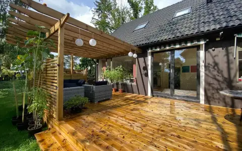 Trall med synliga skruvar kan vara en nackdel för utseendet. Här en altan med pergola, utemöbler och solrosor.