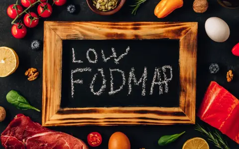 Na tablicy napis "LOW FODMAP". Wokół świeże produkty: mięso, ryba, pomidorki, cytryna, jajko, papryka, orzechy, jagody, szpinak.