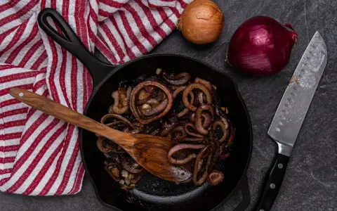 Cipolle in agrodolce caramellate in padella, pronte per essere gustate. Accanto, cipolle fresche e un coltello affilato.