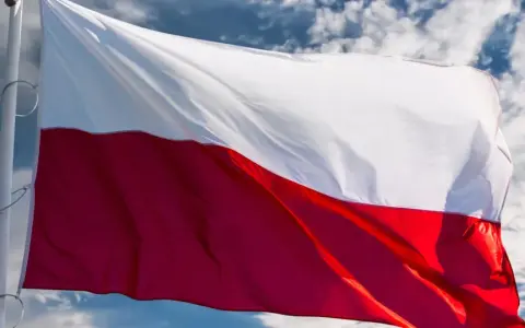 Flaga biało-czerwona powiewa na wietrze na tle błękitnego nieba z chmurami.