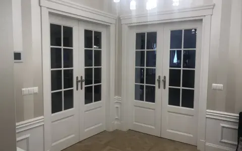 Eleganckie białe drzwi dwuskrzydłowe z przeszkleniem, osadzone w metalowych futrynach, tworzą stylowe przejście.