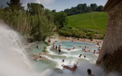 Persone si rilassano nelle cascate naturali delle **Terme di Saturnia**, immerse nel verde della campagna toscana.