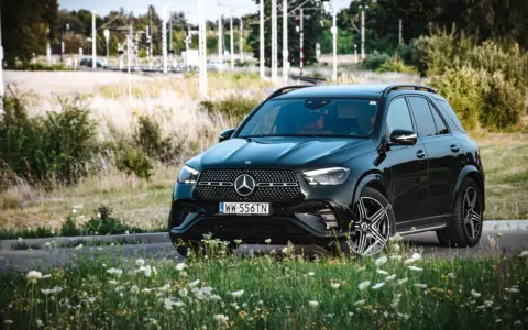 Czarny Mercedes GLE 350 z czerwonym wnętrzem zaparkowany na tle łąki i torów kolejowych.