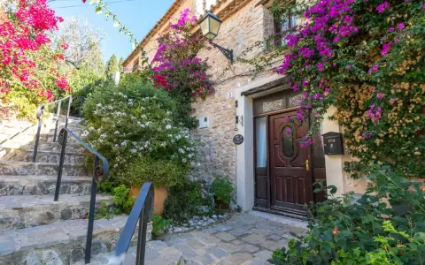 Escaleras de piedra adornadas con buganvillas y flores blancas, que llevan a la entrada de una casa de piedra. Un ejemplo de los pueblos bonitos de Alicante.