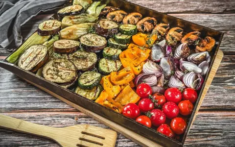 Buntes Gemüse wie Auberginen, Zucchini, Paprika, Zwiebeln und Tomaten auf einem Blech für ein köstliches vegetarisches Grillen.