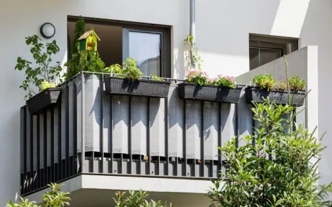 Balcone condominio con fioriere e telo grigio per creare idee privacy. Un nido per uccelli decora la vegetazione.