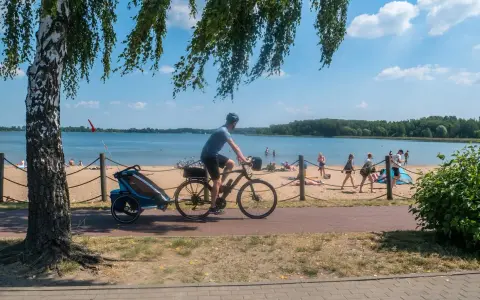 Mężczyzna na rowerze z przyczepką jedzie ścieżką rowerową wzdłuż plaży. To idealne miejsce na wycieczkę trasą pogoria 3.