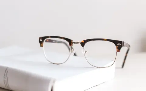Okulary z oprawkami w stylu clubmaster leżą na białej książce. Czy wada 0.75 to powód, by nosić okulary?