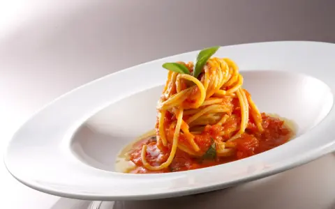 Un nido di spaghetti conditi con una salsa rossa vibrante di pomodorini freschi, guarnito con foglie di basilico verde brillante, servito in un piatto bianco elegante.