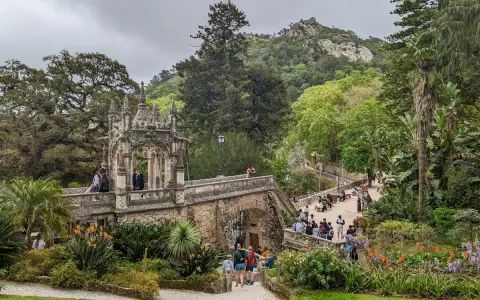 Ein märchenhafter Sintra Garten mit einer steinernen Brücke, üppiger Vegetation und Besuchern, die die Aussicht genießen.