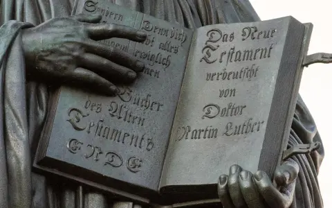 Hände halten ein aufgeschlagenes Buch mit Luthers Übersetzung des Neuen Testaments. Die Bedeutung der Reformation wird durch diese Darstellung greifbar.