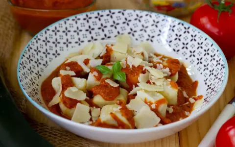 Gnocchi ziemniaczane w sosie pomidorowym, posypane parmezanem. Obok pomidor i cukinia.