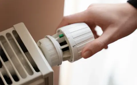 Dłoń kręci termostatem grzejnika. Kaloryfer nie grzeje, a nie jest zapowietrzony, co frustruje domowników.