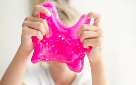 Dziecko bawi się różowym slime, który wygląda jak z przepisu na domowy slime.