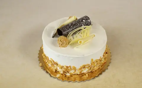 Elegancki tort rafaello z wiórkami migdałowymi, czekoladową rurką i dekoracjami z białej czekolady.