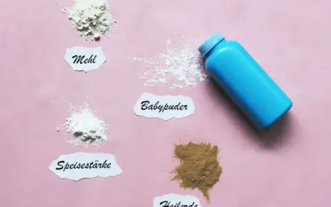 Blauer Behälter mit Babypuder, daneben Häufchen von Mehl, Speisestärke und Heilerde. Babypuder als trockenshampoo für schnelle Hilfe.