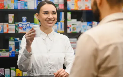 Uśmiechnięty farmaceuta podaje klientowi białe opakowanie leku.