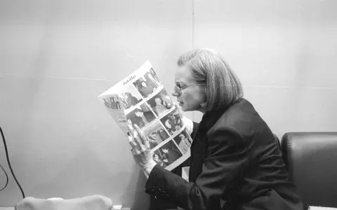 Fleur Jaeggy, con occhiali e giacca scura, legge un giornale con foto.
