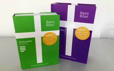 Zwei "Basis Bibel" Ausgaben, eine grüne und eine violette, mit dem Aufdruck "NEU Altes + Neues Testament". Diese evangelische Bibel ist so gestaltet, dass sie leicht verständlich ist.