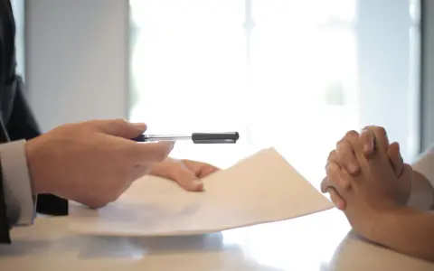 Man en traje entrega documento a persona con manos entrelazadas, discutiendo cómo devolver fianza alquiler antes finalizar contrato.