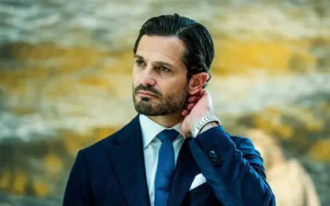 Prins Carl Philip i mörkblå kostym, vit skjorta och blå slips. Hans hand vilar bakom örat, en detalj som speglar hans intresse för carl philip design.