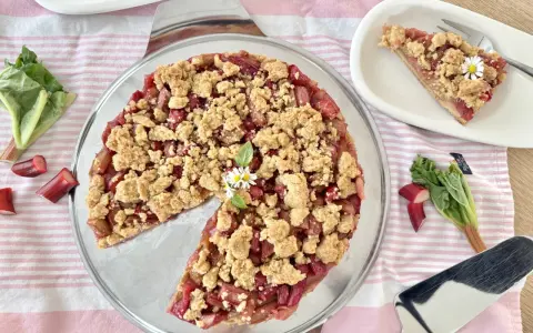Ein köstlicher Rhabarber Streuselkuchen mit frischem Rhabarber und knusprigen Streuseln, garniert mit kleinen Gänseblümchen.