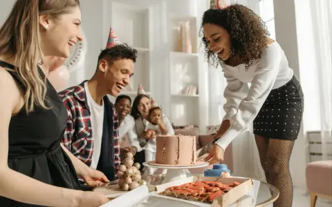 Fröhliche Gruppe feiert den 30. Geburtstag mit Kuchen und Keksen. Alle tragen Partyhüte und lachen ausgelassen.