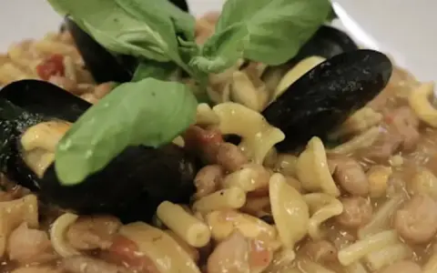 Un piatto invitante di pasta fagioli e cozze, guarnito con foglie di basilico fresco.