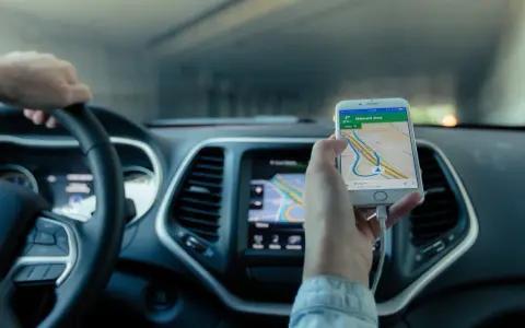Mano al volante, móvil con mapa GPS mostrando cómo funciona un localizador GPS para coche.